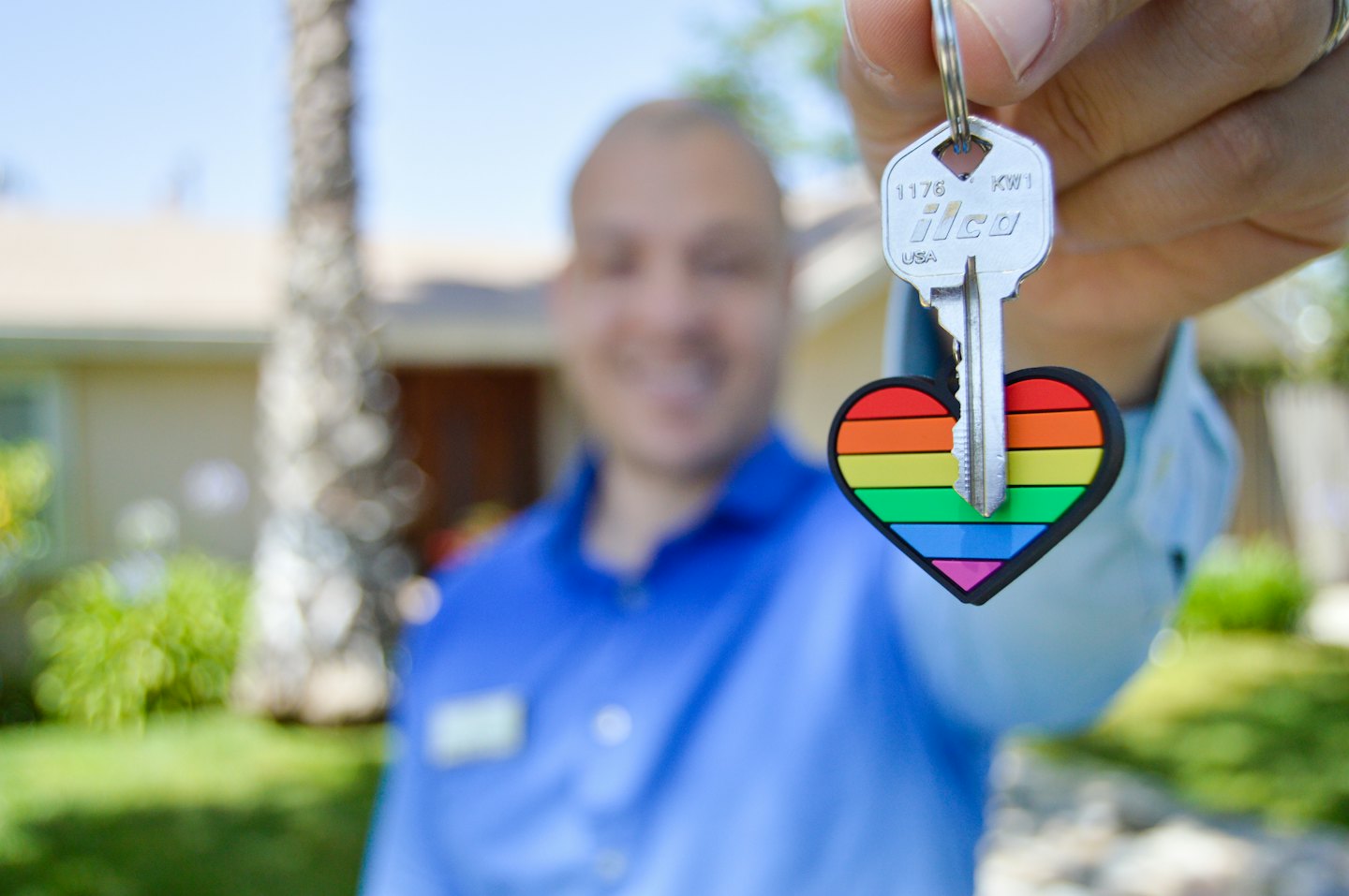 Persona che tiene una chiave di casa con un portachiavi a forma di cuore arcobaleno.